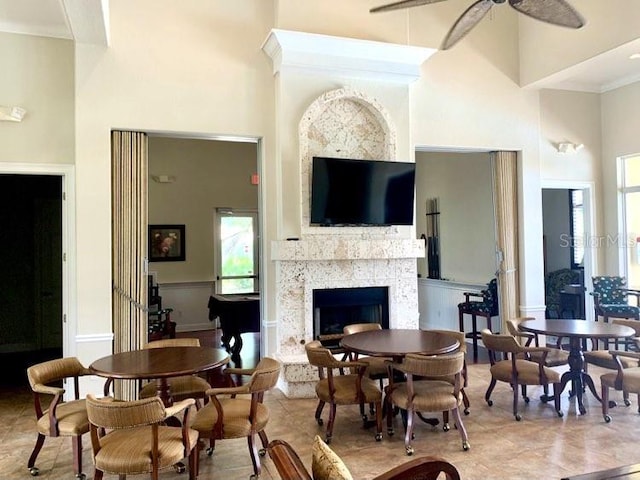 interior space featuring ceiling fan, ornamental molding, light tile patterned floors, a high ceiling, and a fireplace