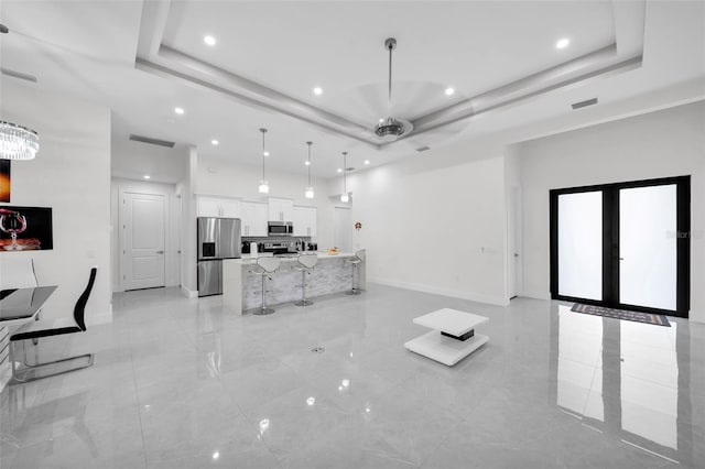 unfurnished living room with ceiling fan, a tray ceiling, and french doors