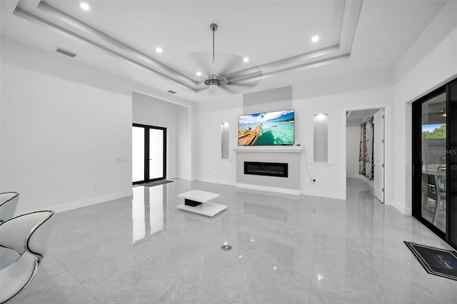 unfurnished living room with a tray ceiling, ceiling fan, and french doors