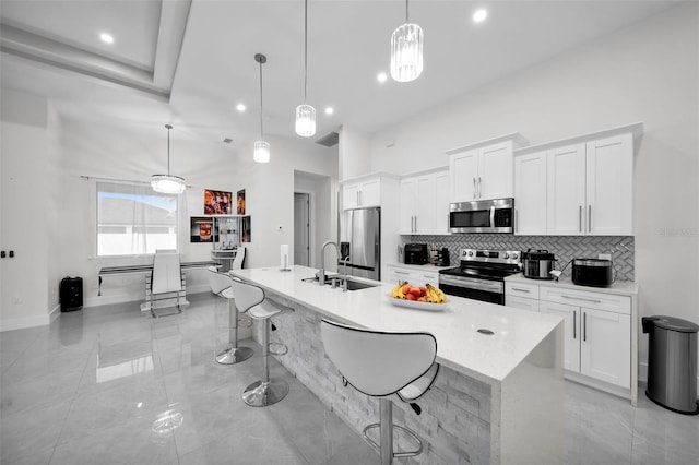 kitchen with white cabinets, a center island with sink, stainless steel appliances, and hanging light fixtures