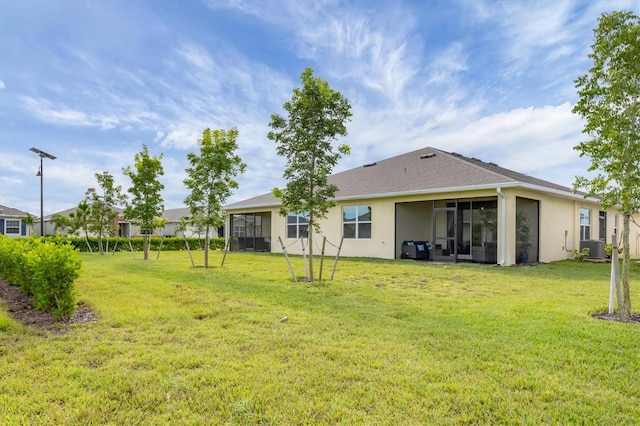 rear view of house featuring a sunroom, a lawn, central air condition unit, and stucco siding