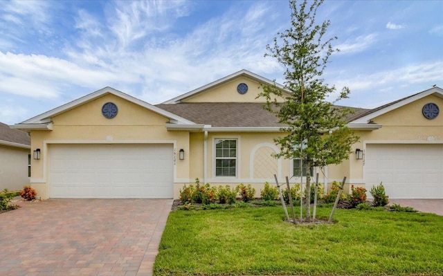 ranch-style house with decorative driveway, stucco siding, a shingled roof, an attached garage, and a front yard