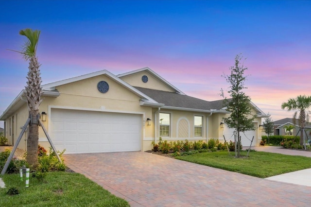 ranch-style house featuring decorative driveway, a lawn, an attached garage, and stucco siding