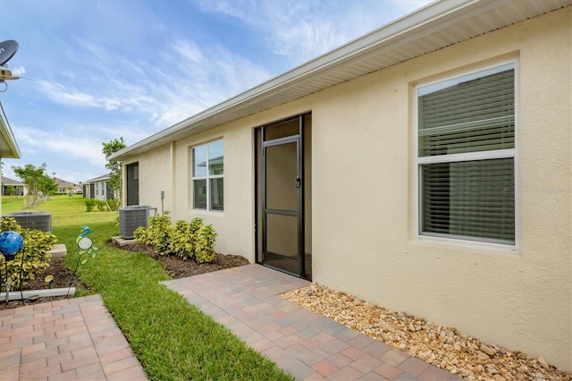 property entrance featuring a patio area, a yard, central AC unit, and stucco siding