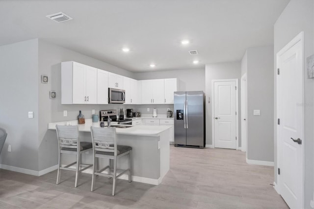 kitchen with stainless steel appliances, a peninsula, white cabinets, light countertops, and a kitchen bar