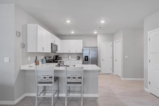 kitchen featuring a peninsula, stainless steel appliances, white cabinetry, and light countertops