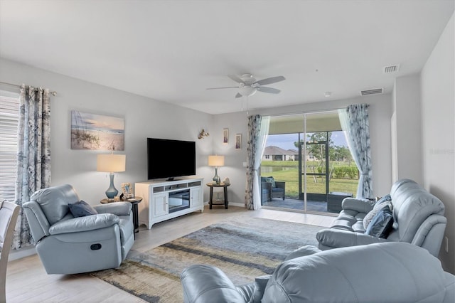 living room with light wood finished floors, visible vents, and a ceiling fan