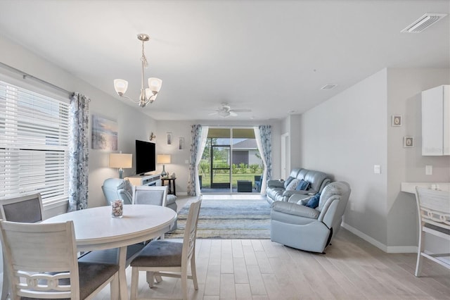 living area featuring visible vents, light wood-style flooring, baseboards, and ceiling fan with notable chandelier