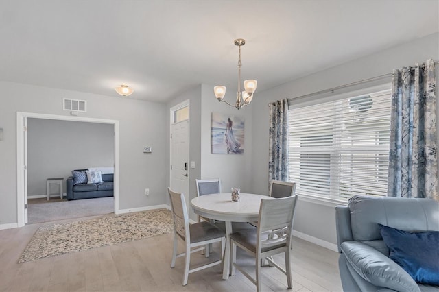 dining room with baseboards, light wood-style floors, visible vents, and a notable chandelier