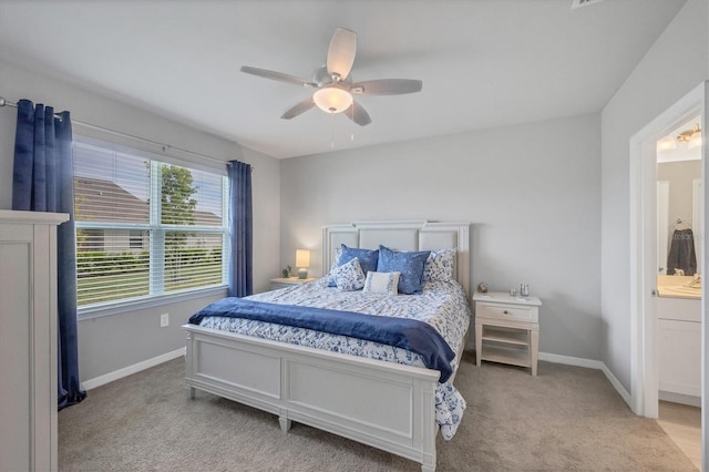 bedroom featuring light carpet, ceiling fan, baseboards, and ensuite bathroom