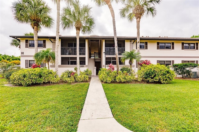 view of front of property featuring a balcony, a front lawn, and central air condition unit