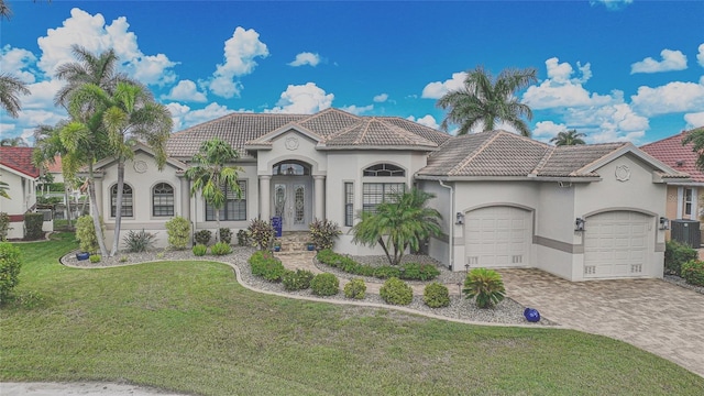 mediterranean / spanish home with a garage, central air condition unit, and a front lawn