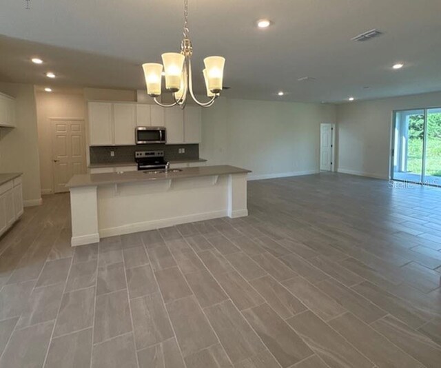 kitchen with pendant lighting, a center island with sink, a chandelier, white cabinetry, and stainless steel appliances