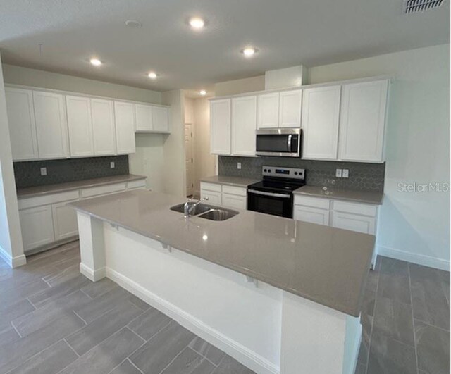 kitchen with a kitchen island with sink, sink, white cabinets, backsplash, and appliances with stainless steel finishes