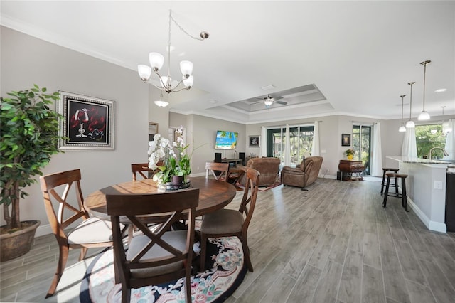 dining area featuring ceiling fan with notable chandelier, a raised ceiling, crown molding, sink, and light hardwood / wood-style floors