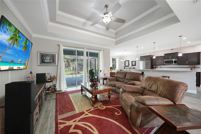 living room with light wood-type flooring, a tray ceiling, ceiling fan, and crown molding