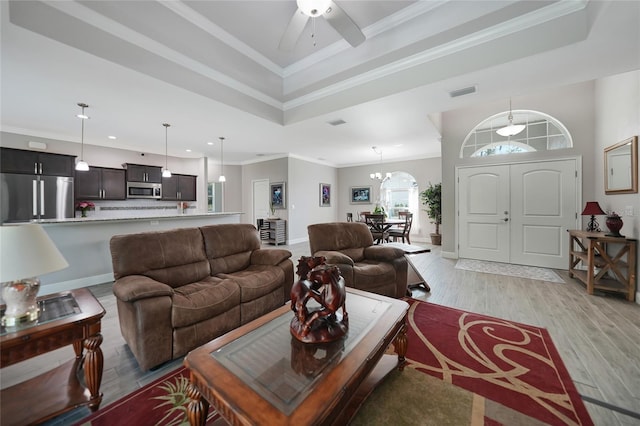 living room with ceiling fan with notable chandelier, ornamental molding, and light hardwood / wood-style flooring