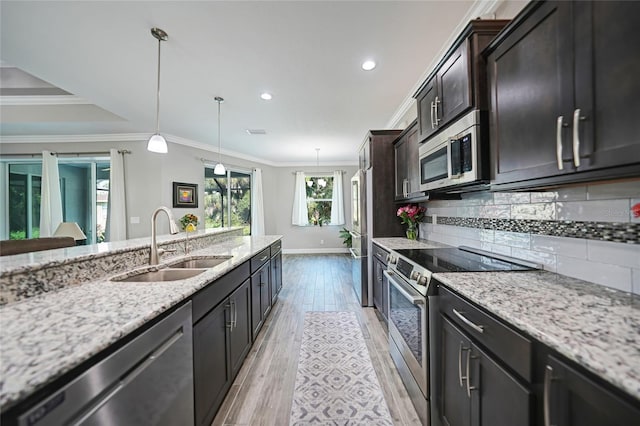 kitchen featuring light stone countertops, sink, stainless steel appliances, crown molding, and decorative light fixtures