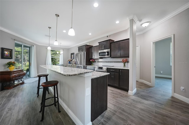 kitchen with a kitchen bar, backsplash, stainless steel appliances, decorative light fixtures, and an island with sink