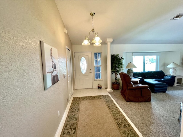 entrance foyer with a chandelier, ornate columns, light carpet, and vaulted ceiling