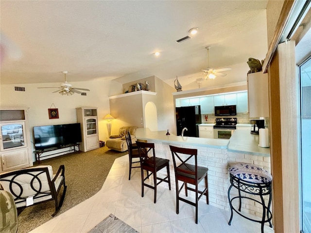 kitchen with lofted ceiling, black appliances, a kitchen breakfast bar, light tile patterned flooring, and kitchen peninsula