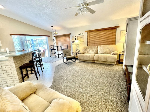 living room with a brick fireplace, a textured ceiling, ceiling fan, lofted ceiling, and light tile patterned flooring