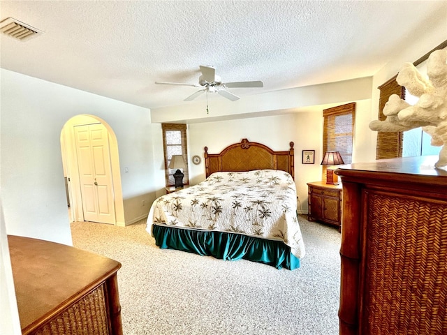 bedroom with ceiling fan, light colored carpet, and a textured ceiling