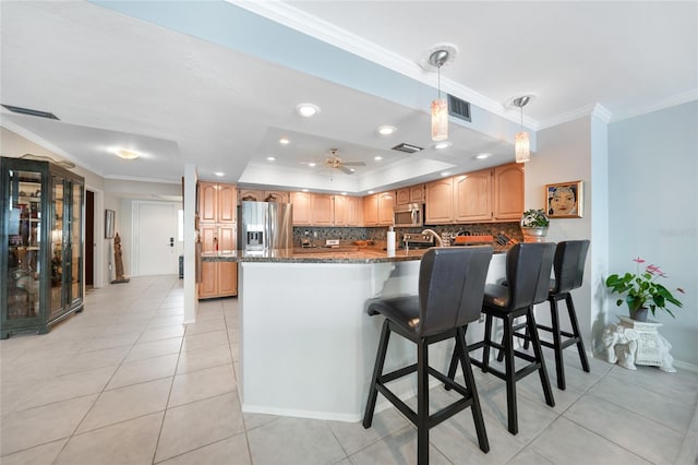 kitchen with light tile patterned floors, ornamental molding, appliances with stainless steel finishes, a kitchen breakfast bar, and dark stone countertops