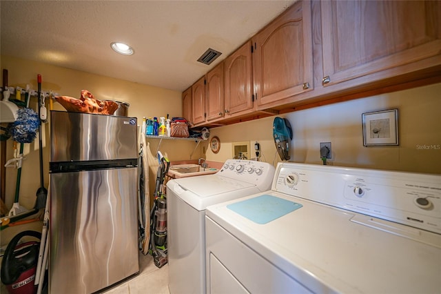 laundry area with cabinets, a textured ceiling, light tile patterned floors, and washing machine and dryer