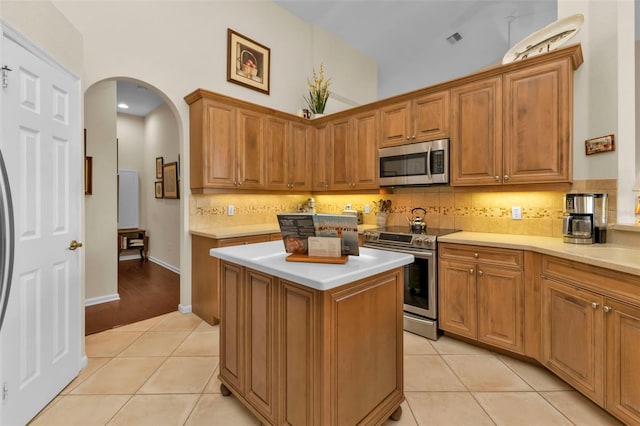 kitchen featuring light tile patterned flooring, a towering ceiling, backsplash, stainless steel appliances, and a center island