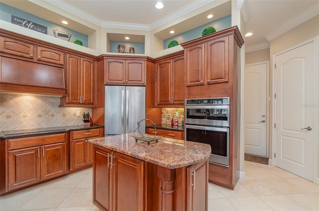 kitchen featuring light tile patterned flooring, stainless steel appliances, dark stone countertops, ornamental molding, and a kitchen island with sink