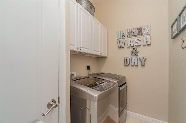 clothes washing area with cabinets, washing machine and clothes dryer, and light tile patterned floors