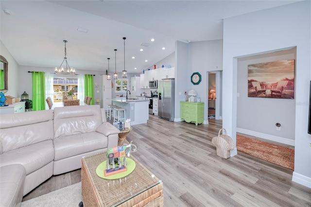 living room with light wood-type flooring, sink, a chandelier, and high vaulted ceiling