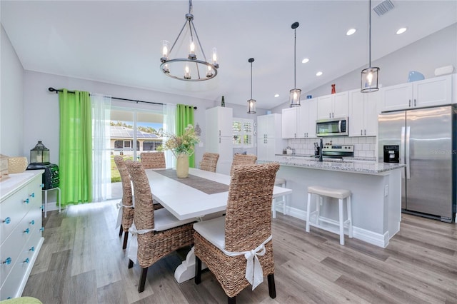 dining room featuring an inviting chandelier, light wood-type flooring, and vaulted ceiling