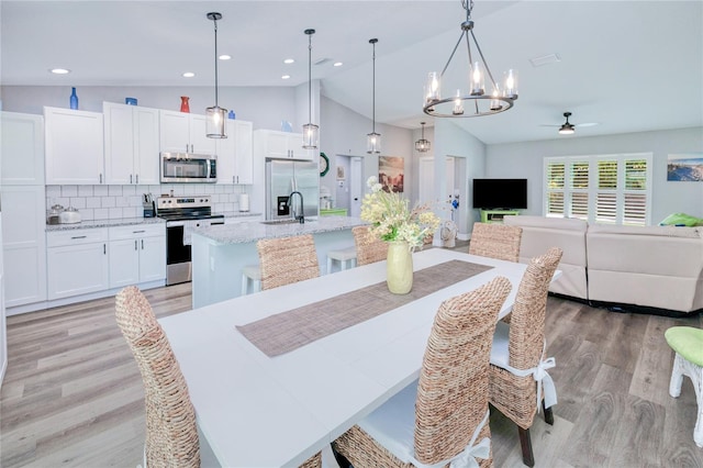 dining space with ceiling fan with notable chandelier, lofted ceiling, sink, and light hardwood / wood-style flooring