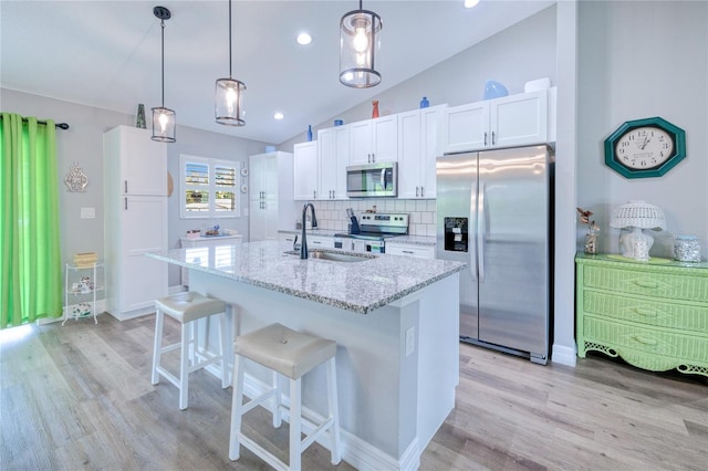 kitchen featuring appliances with stainless steel finishes, vaulted ceiling, light stone counters, white cabinets, and light hardwood / wood-style flooring