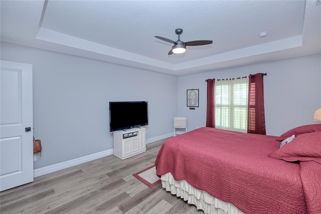 bedroom with light wood-type flooring, a raised ceiling, and ceiling fan