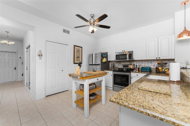 kitchen with appliances with stainless steel finishes, backsplash, white cabinets, and decorative light fixtures