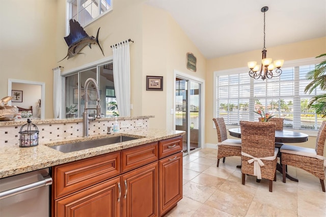 kitchen featuring hanging light fixtures, light stone counters, dishwasher, sink, and a chandelier