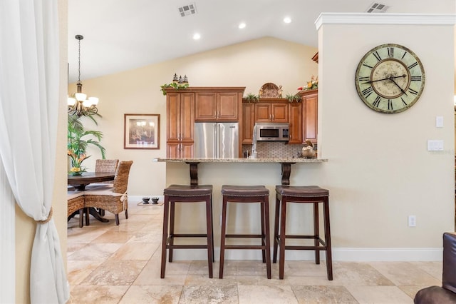 kitchen with decorative light fixtures, a kitchen breakfast bar, appliances with stainless steel finishes, light stone countertops, and vaulted ceiling