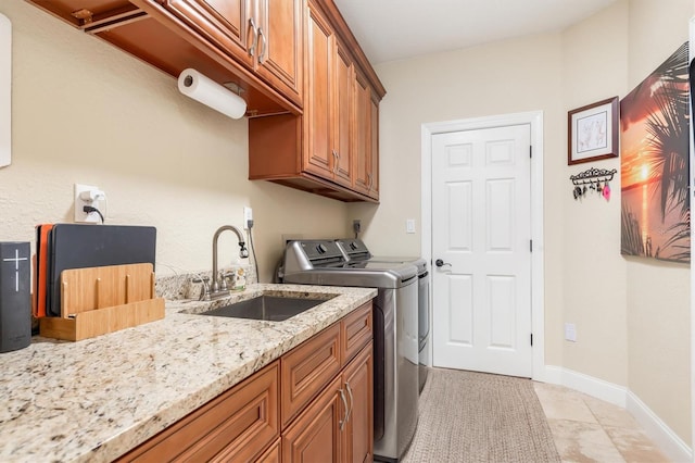 clothes washing area featuring washer and clothes dryer, sink, light tile patterned floors, and cabinets