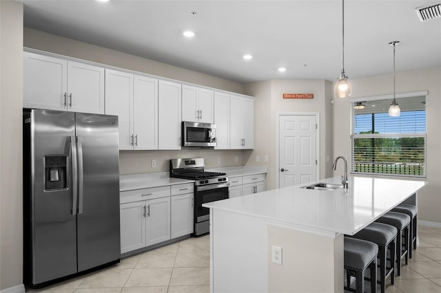 kitchen with white cabinets, sink, a center island with sink, decorative light fixtures, and appliances with stainless steel finishes