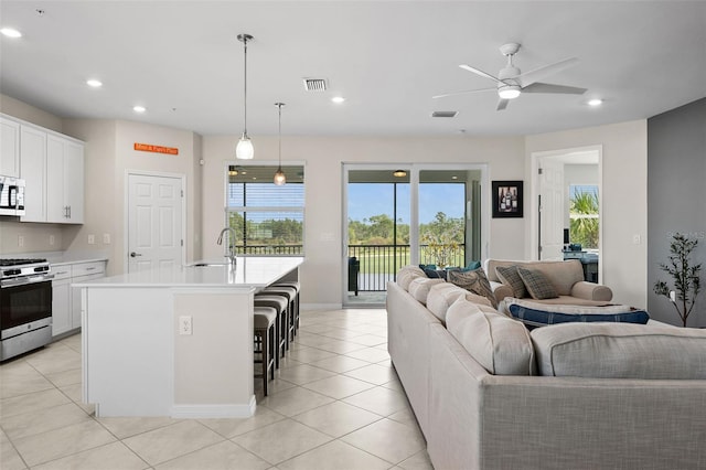 kitchen with white cabinets, a kitchen breakfast bar, a center island with sink, appliances with stainless steel finishes, and decorative light fixtures