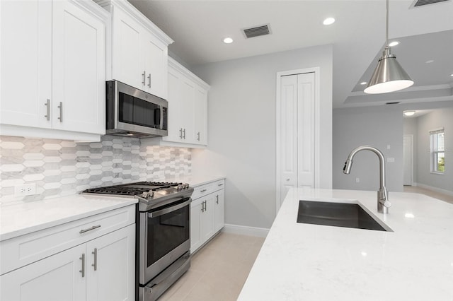 kitchen featuring light stone counters, sink, white cabinetry, hanging light fixtures, and stainless steel appliances