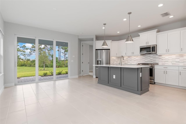 kitchen featuring pendant lighting, a kitchen island with sink, tasteful backsplash, white cabinets, and appliances with stainless steel finishes