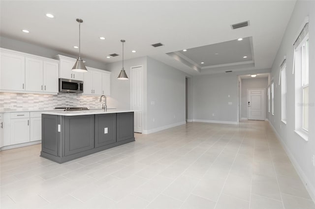 kitchen featuring pendant lighting, a kitchen island with sink, tasteful backsplash, white cabinetry, and appliances with stainless steel finishes