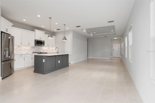 kitchen with pendant lighting, a kitchen island with sink, stainless steel appliances, and white cabinetry