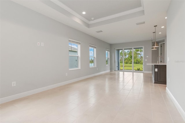 empty room with a raised ceiling, light tile patterned flooring, sink, and a wealth of natural light