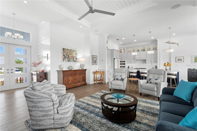 living room with a towering ceiling, ceiling fan with notable chandelier, dark hardwood / wood-style flooring, a tray ceiling, and french doors