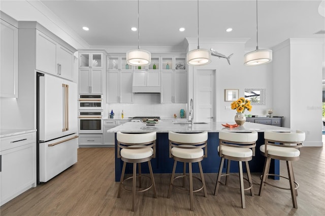 kitchen featuring decorative light fixtures, a center island with sink, dark hardwood / wood-style floors, and built in fridge